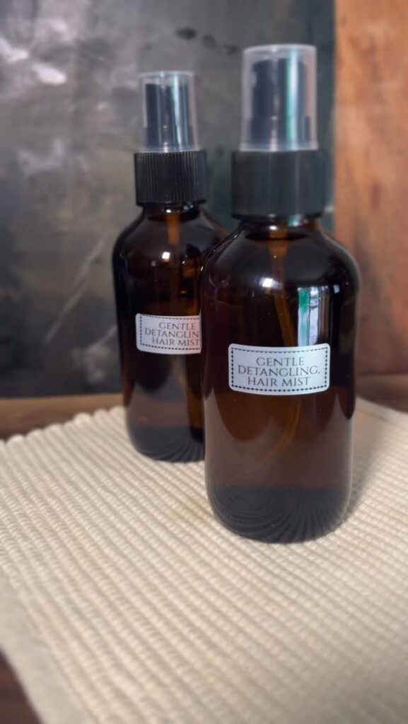 Two amber glass spray bottles labeled as gentle detangling hair mist on white fabric.