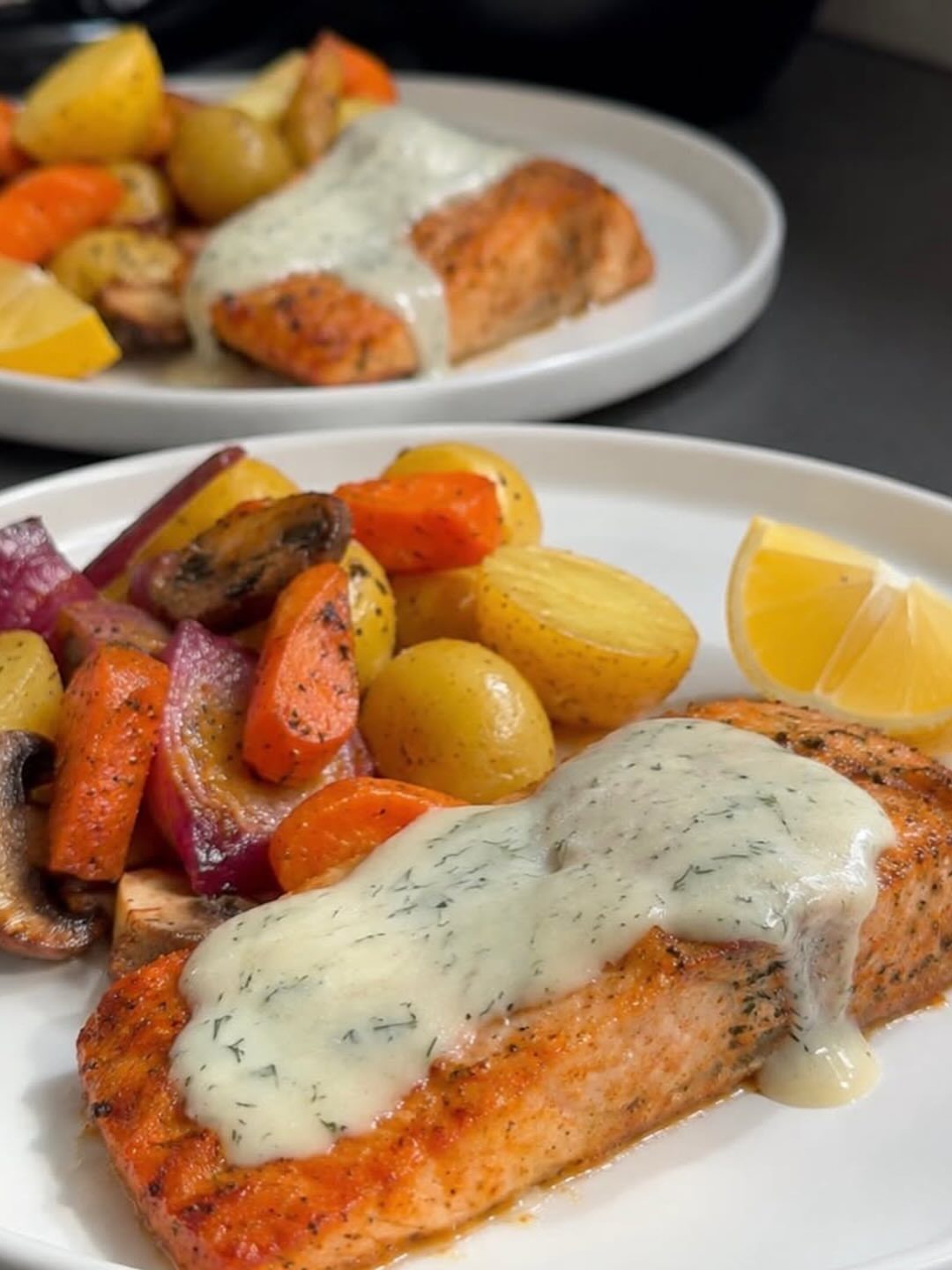 Cooked salmon fillet with creamy sauce, roasted vegetables, and a lemon wedge.