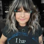 Woman with wavy gray and brown blended highlights and colorful glasses.