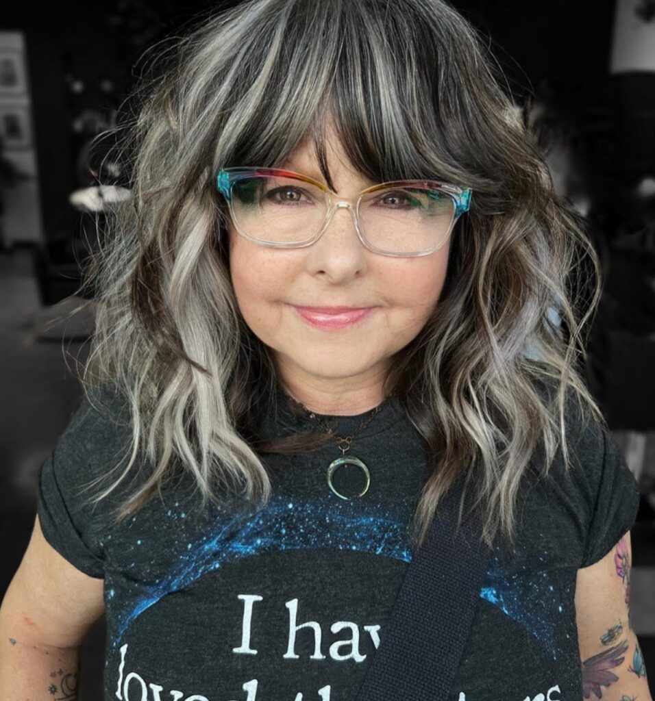 Woman with wavy gray and brown blended highlights and colorful glasses.