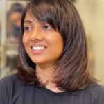 Woman with dark brown shoulder-length hair and a side-swept fringe smiling.