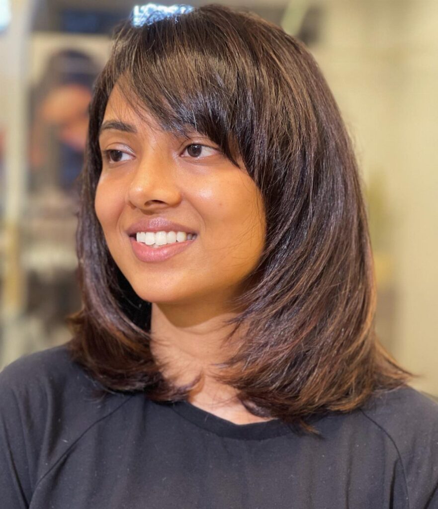Woman with dark brown shoulder-length hair and a side-swept fringe smiling.