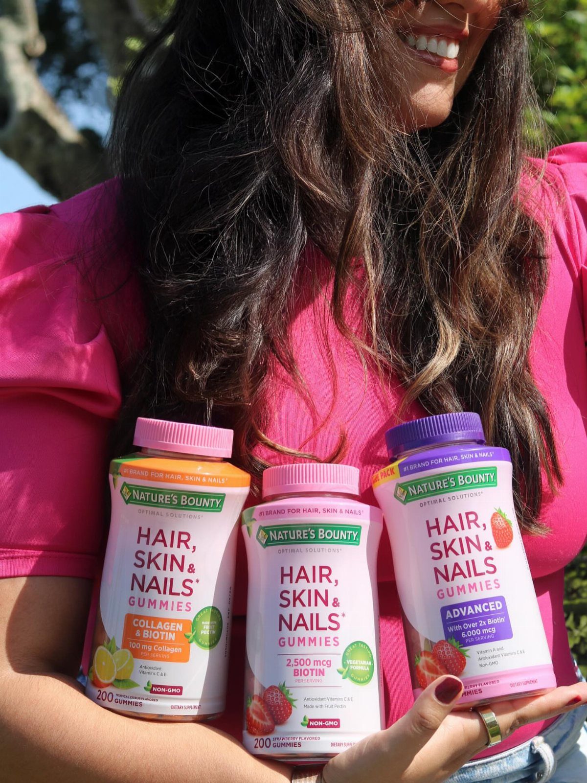 Woman holding three different bottles of hair, skin, and nails gummy vitamins.