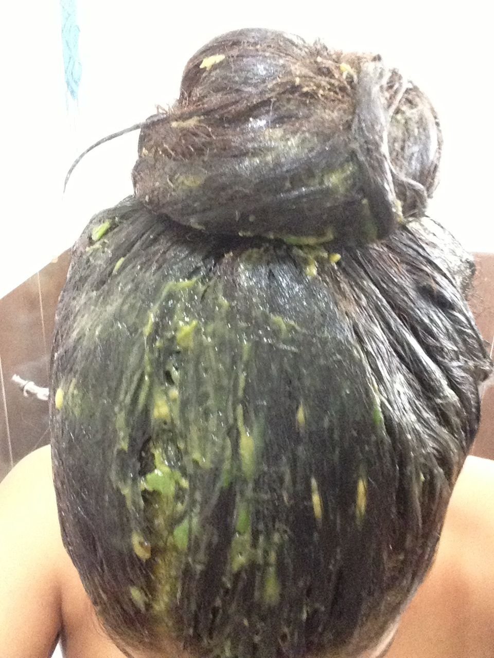 Dark hair tied in a bun covered in a thick green hair mask