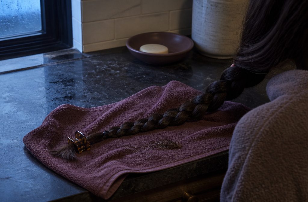 Dark hair parted over a damp scalp with clear serum and a glass dropper nearby