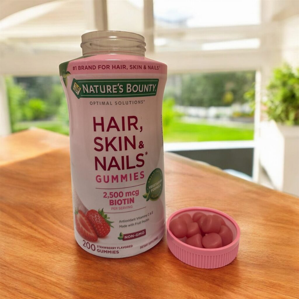 Nature's Bounty Biotin gummies bottle and red gummies in a small pink bowl.