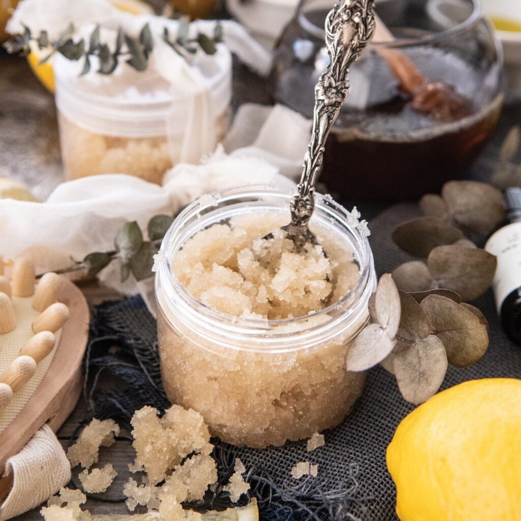Beige salt scrub in a clear jar with a silver spoon and lemon.