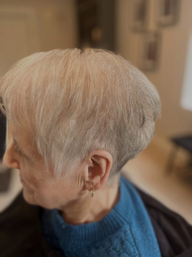 Older woman with a short, thinning grey hairstyle wearing a blue sweater.